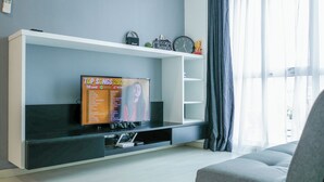 A modern living room with a flat-screen TV on a white entertainment unit, a grey sofa, and a window with sheer curtains.