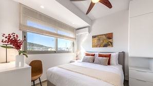 Ein modernes Schlafzimmer mit einem großen Bett, einem Schreibtisch, einem Stuhl und einem Fenster mit Blick auf die Stadt.