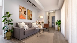 Ein modernes Wohnzimmer mit einem grauen Sofa, einem kleinen runden Tisch und einer Topfpflanze.