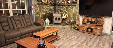 A cozy living room with a stone wall, a fireplace, a sofa, a wooden coffee table, and a television.