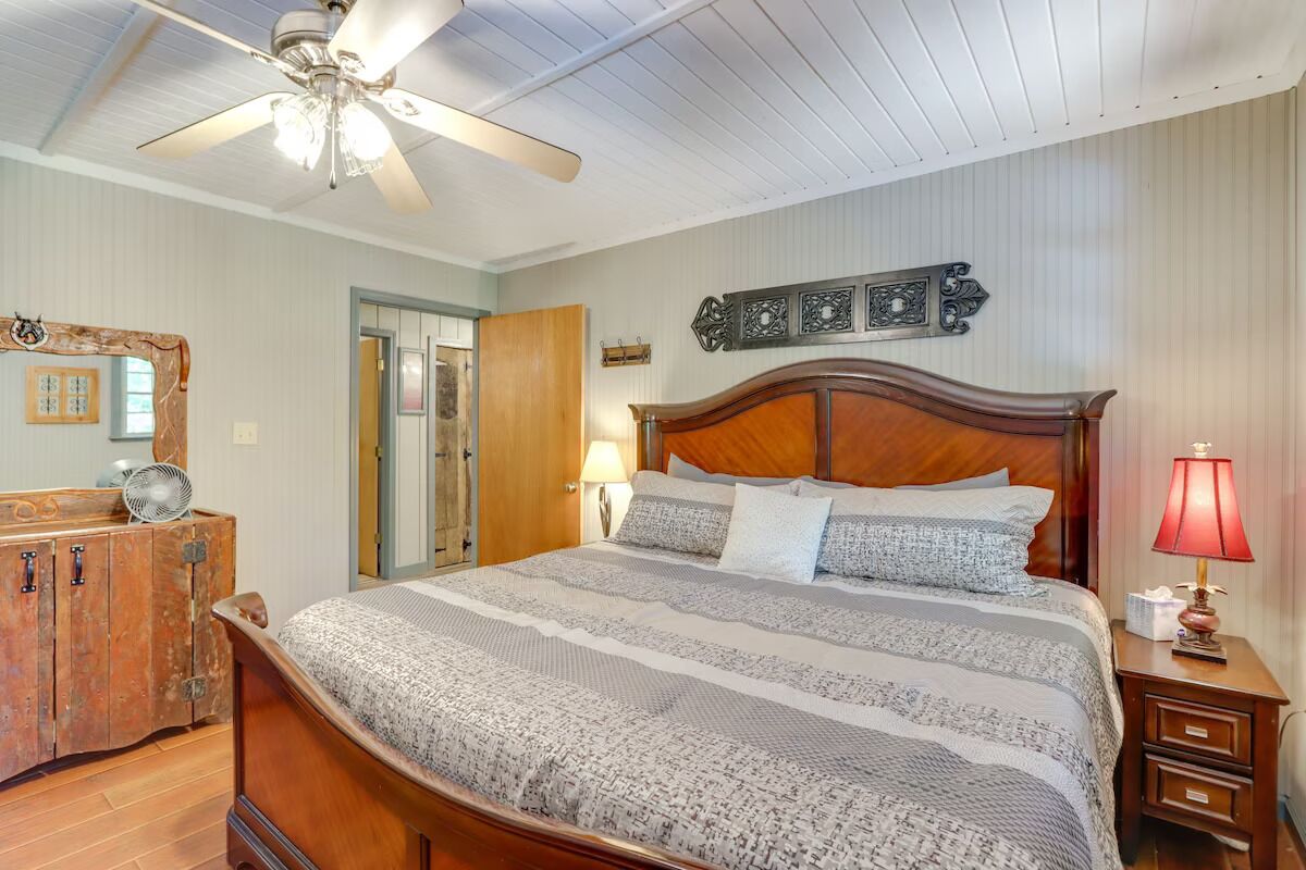 A bedroom with a wooden bed, a ceiling fan, a wooden dresser, and a nightstand with a lamp.
