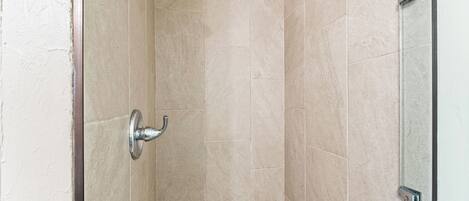 Une douche aux carreaux beiges et dotée d’un pommeau de douche chromé.