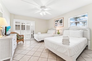 A hotel room with two beds, a ceiling fan, a wicker chair, and a large window with blinds. - Crescent Arms by Beachside Management (Siesta Key)