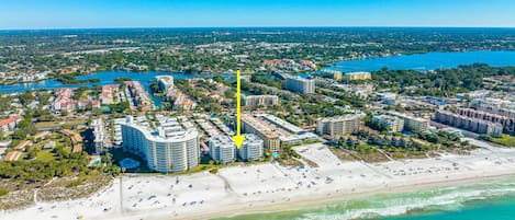 An aerial view of a coastal city with a prominent hotel complex, beachfront, and surrounding urban area.