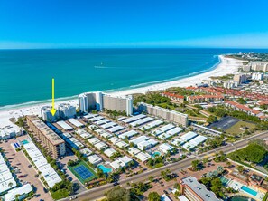 Vista aérea de um hotel à beira-mar, com vários edifícios, uma praia e um estacionamento.