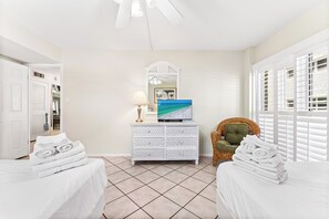 A hotel room with two beds, a white dresser, a television, and a window with blinds.