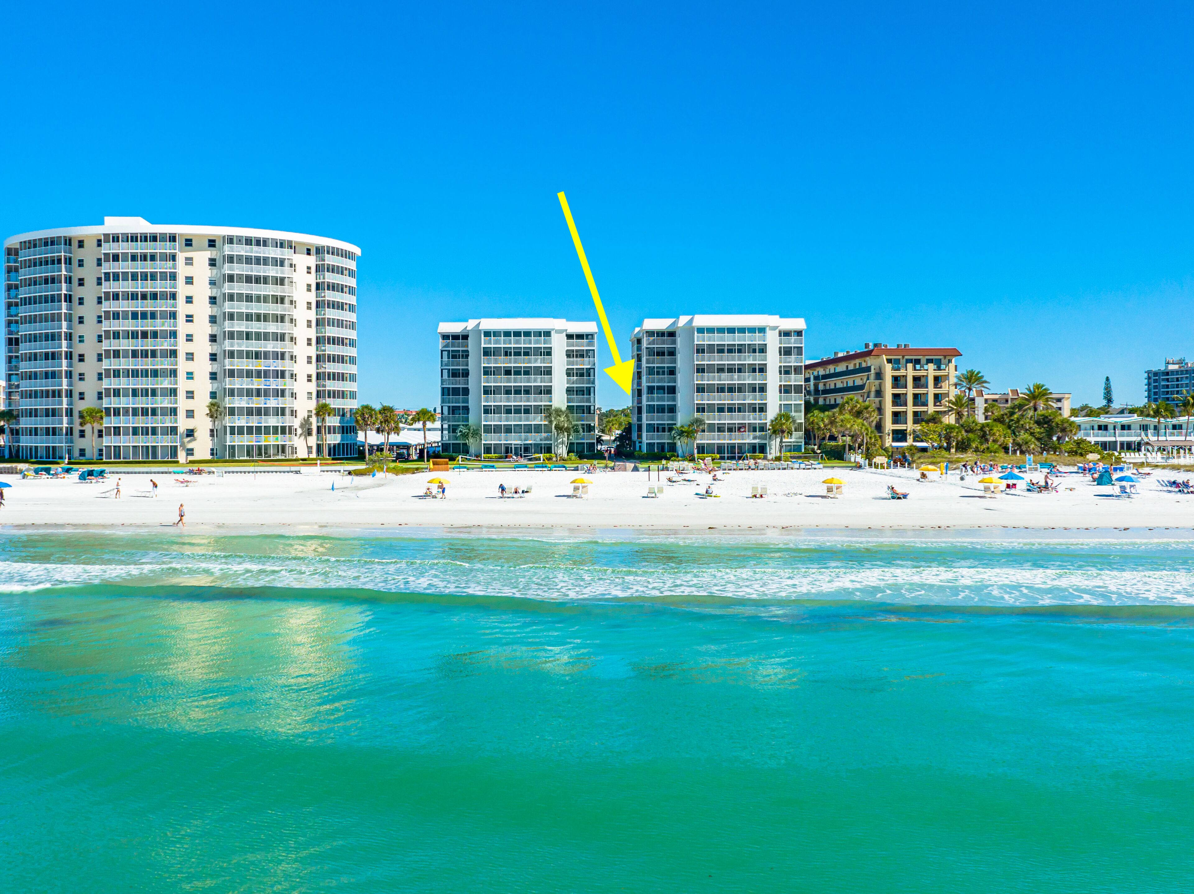 A beachfront hotel with multiple floors, a sandy beach, and palm trees.