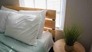A bed with white bedding and a round wooden table with a potted plant beside it. - Cute cottage near the Navy base (Pensacola)