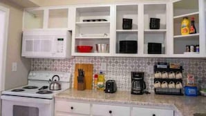 A kitchen with white cabinets, a microwave, a stove, and various kitchen items on the counter. - Cute cottage near the Navy base (Pensacola)
