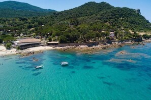 Eine Küstenlandschaft mit klarem türkisblauem Wasser, einem Sandstrand und einem gebirgigen Hintergrund.
