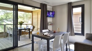 A modern room with a dining table, white chairs, a TV mounted on the wall, and large windows. - Propriano Chalet near Sandy Beaches (Propriano)
