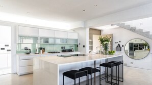 A modern kitchen with a large island, bar stools, and a staircase leading to another level. - 26OnFirst: UPS, Sea Views & Personalised Service (Cape Town)