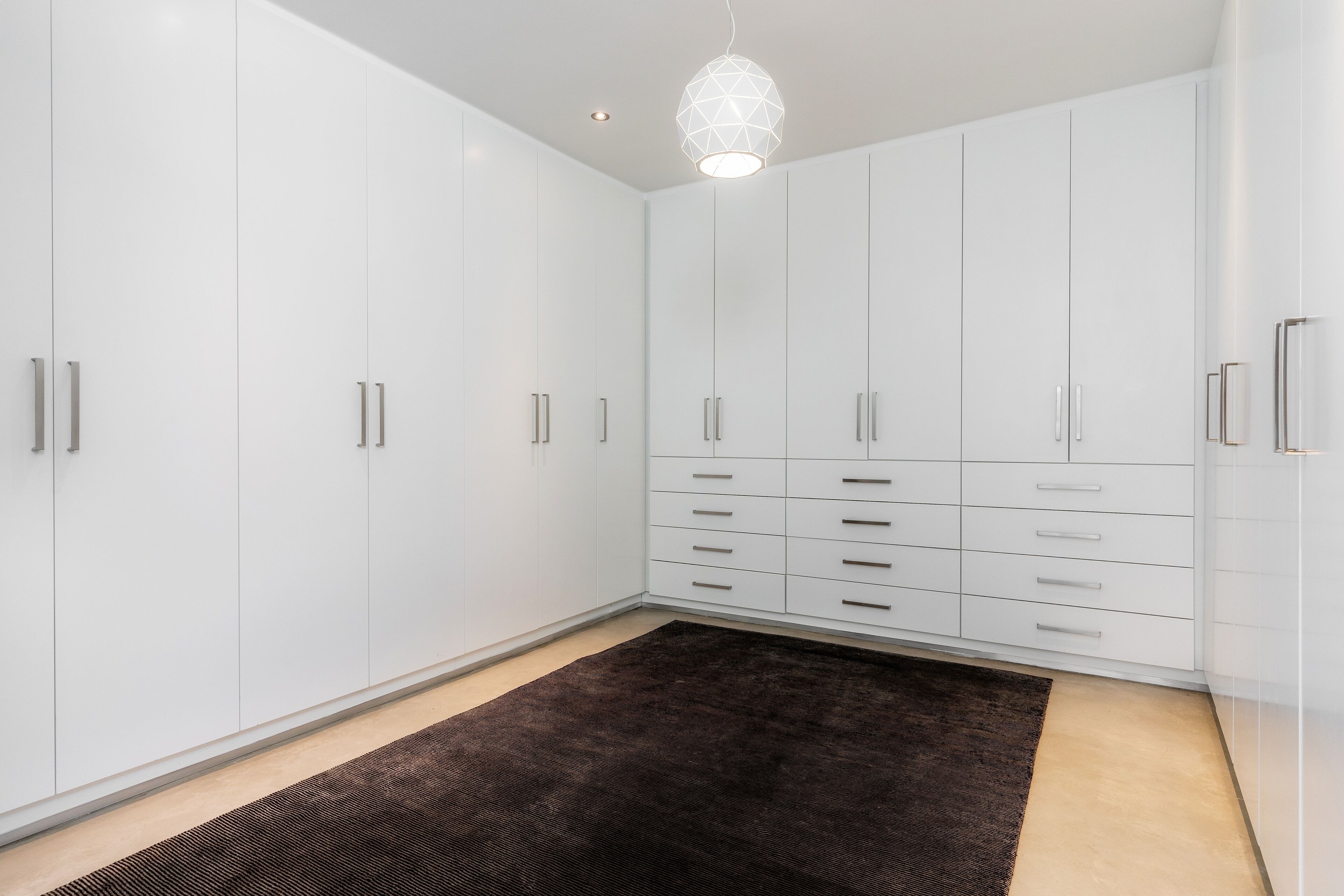 A room with white cabinets, a brown rug, and a geometric pendant light.