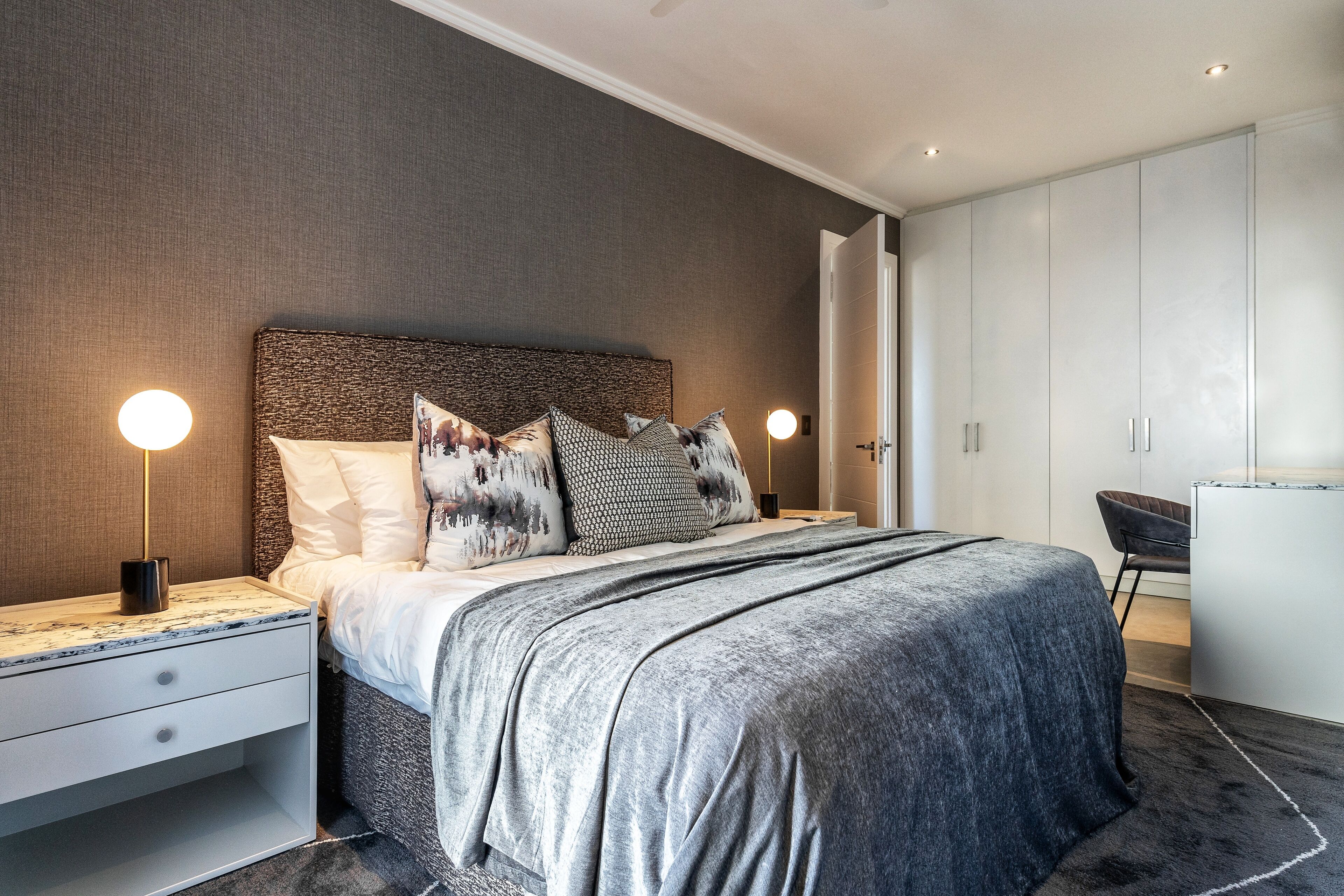 A modern bedroom with a large bed, nightstands, and a wardrobe.