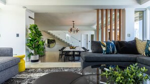 A modern living room with a grey sofa, a coffee table, and a potted plant. There is a staircase leading to an upper level. - 26OnFirst: UPS, Sea Views & Personalised Service (Cape Town)