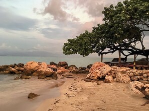 A beach with large rocks, a wooden structure, and a tree.