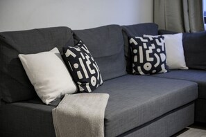 A grey sofa with patterned cushions and a grey throw blanket.