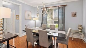 Un coin repas agrémenté d’un lustre, d’une table avec des chaises et d’une fenêtre avec des rideaux.