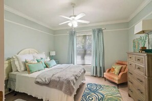 A bedroom with a bed, a ceiling fan, a window with curtains, a chair, and a dresser.