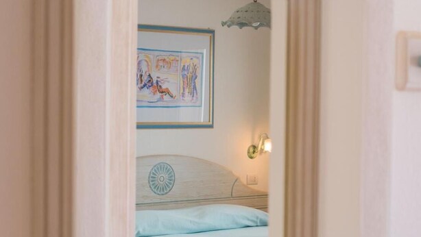 A bedroom with a bed, a wall-mounted light, and a framed picture.