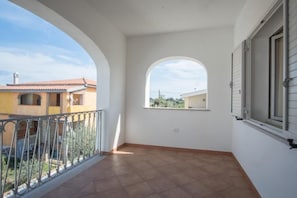 Un balcon avec un sol carrelé, une rambarde en métal et une fenêtre avec des volets.
