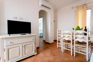 A room with a TV on a cabinet, a dining area with chairs, and a window with curtains. - Superb Le Residenze del Golfo di Orosei No2187 (Orosei)