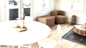 A bright, white interior with a round dining table, white chairs, a wicker basket, and a beige armchair.