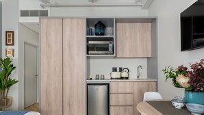 Cocina compacta con microondas, tostadora y lavabo, junto a un comedor con mesa y sillas.