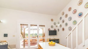 En lys stue med en hvid sofa, et spisebord med stole, et fjernsyn og en trappe med en væg af dekorative tallerkener.