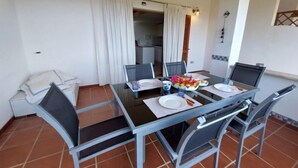 Un comedor con mesa de vidrio y sillas de metal, un sofá blanco y una cocina al fondo.