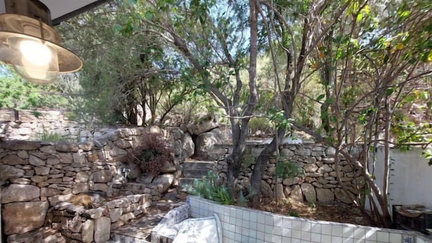 Un área de estar al aire libre con paredes de piedra, un banco de baldosas y una lámpara colgante.