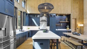 Une cuisine moderne avec des meubles de couleur bleu foncé, des appareils en acier inoxydable et un îlot central doté de tabourets.