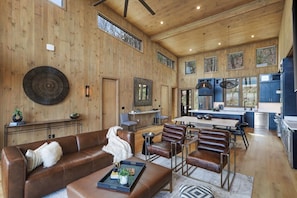 A spacious living room with a brown leather sofa, a coffee table, and a dining area with a large table and chairs. - Luxury Cabin with 5* view, pool, hot tub, fire pit (Blue Ridge)
