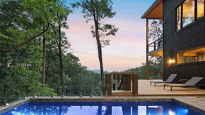 Un espace piscine extérieur moderne, doté d’une terrasse en bois, de chaises longues et offrant une vue sur la forêt environnante.