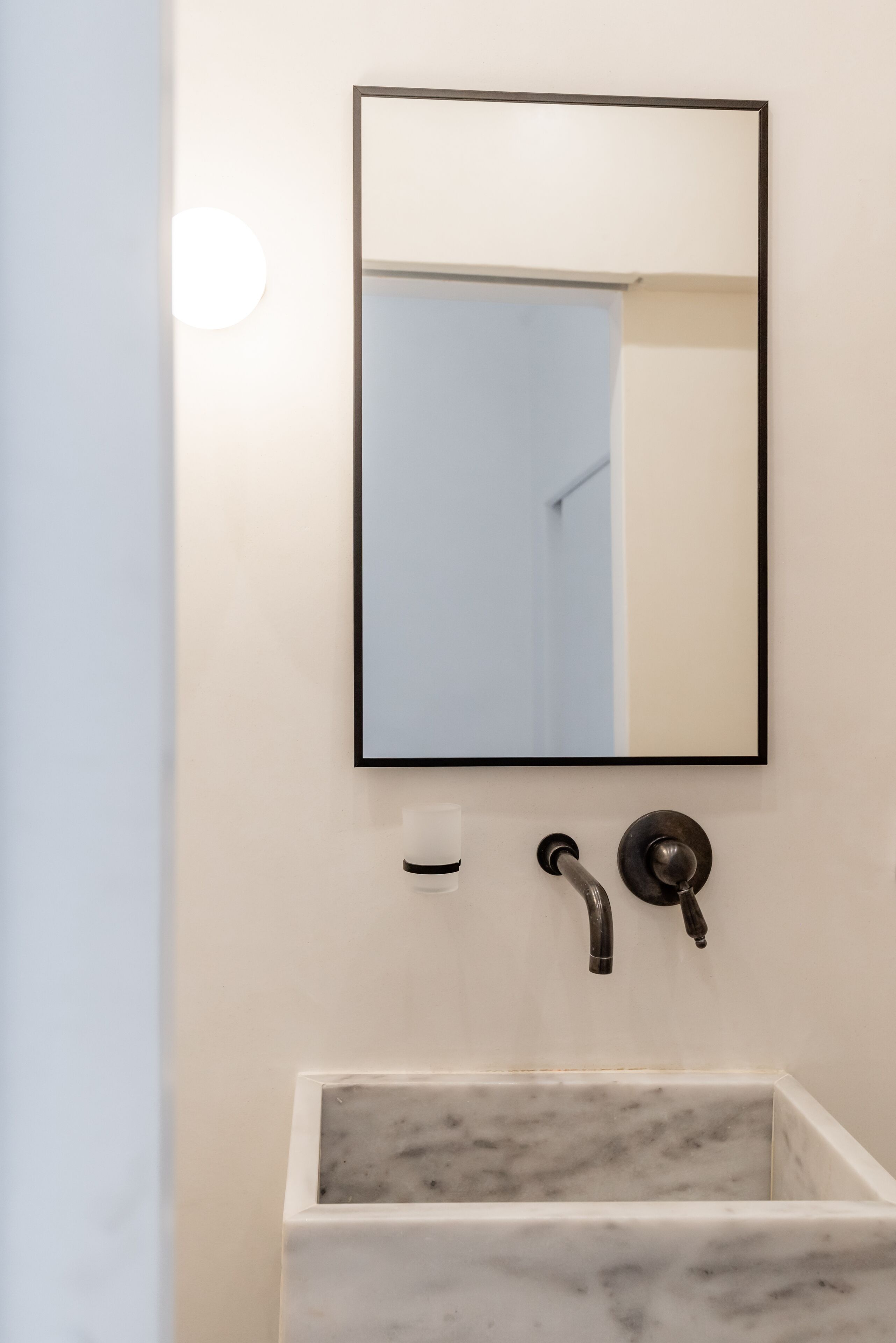 A bathroom with a marble sink, a wall-mounted mirror, and a light fixture.
