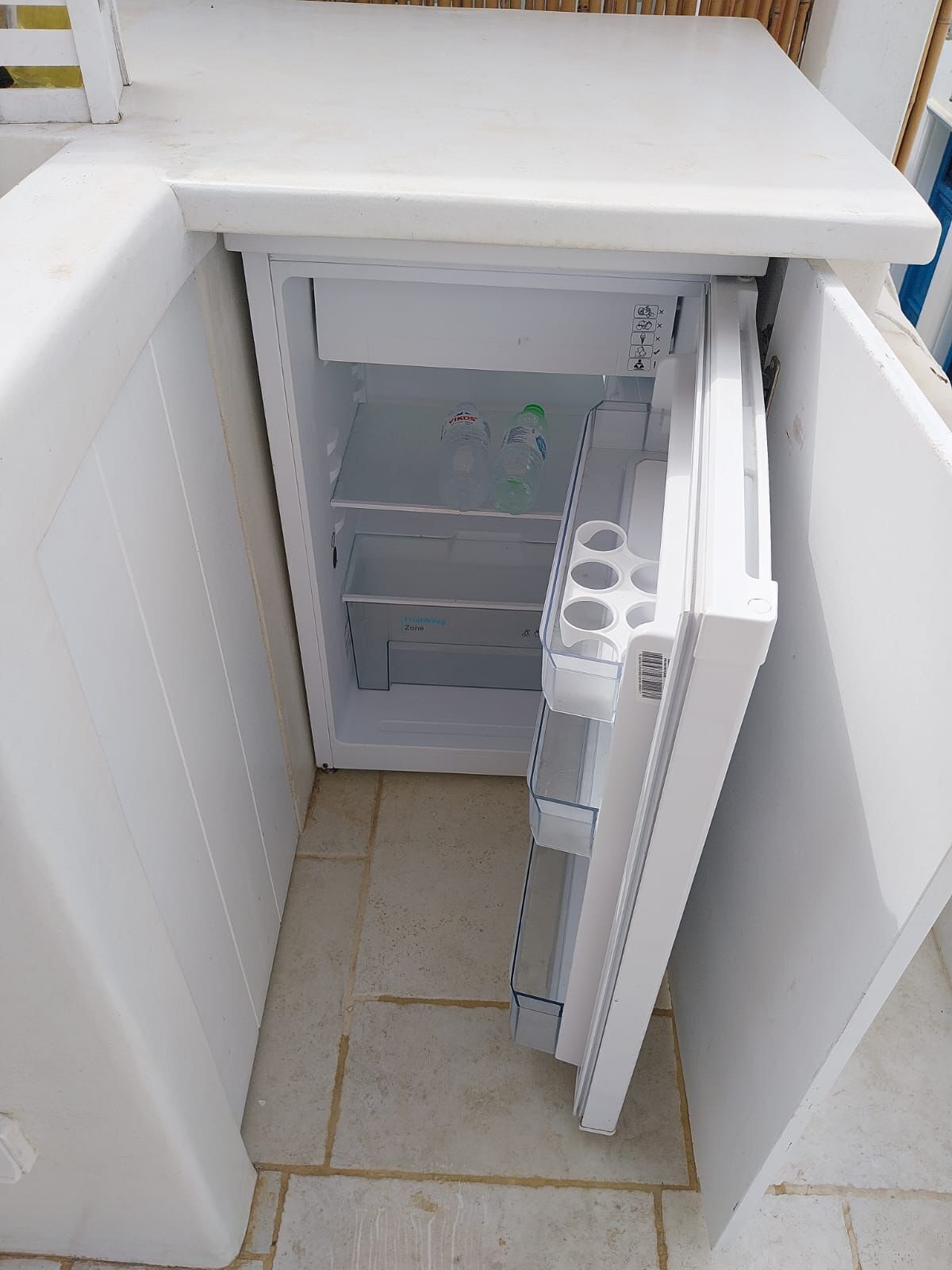 A compact white refrigerator with a freezer compartment, a water dispenser, and a small shelf area.