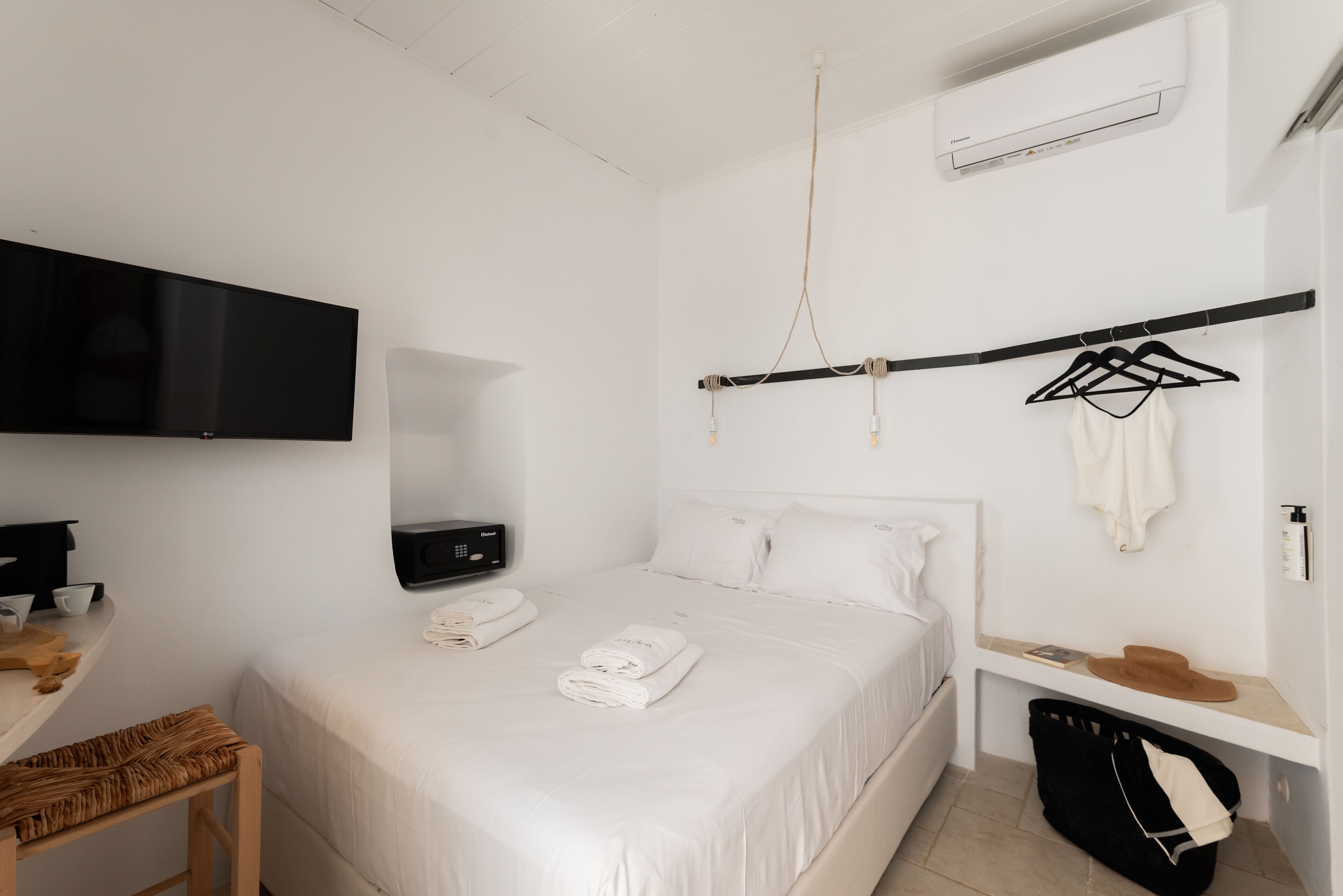 Une chambre d’hôtel comprenant un lit, une télévision, un bureau avec une chaise, un porte-vêtements et une valise.
