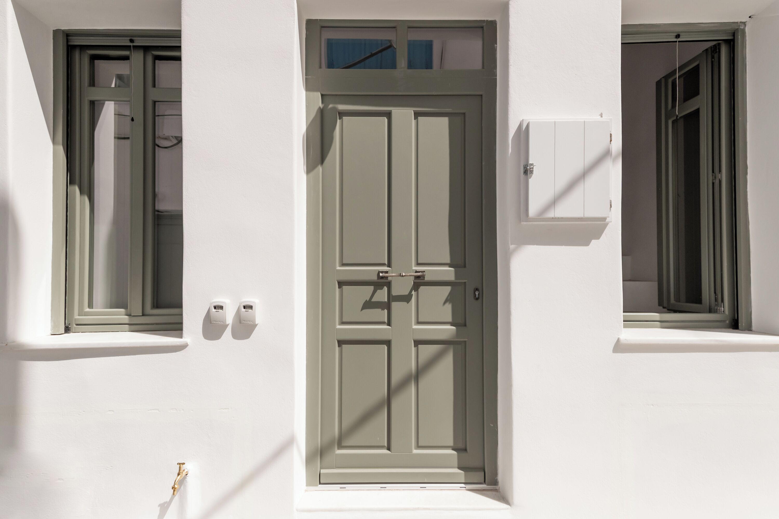 A building facade with a central door, two windows on either side, and a small electrical box on the right wall.