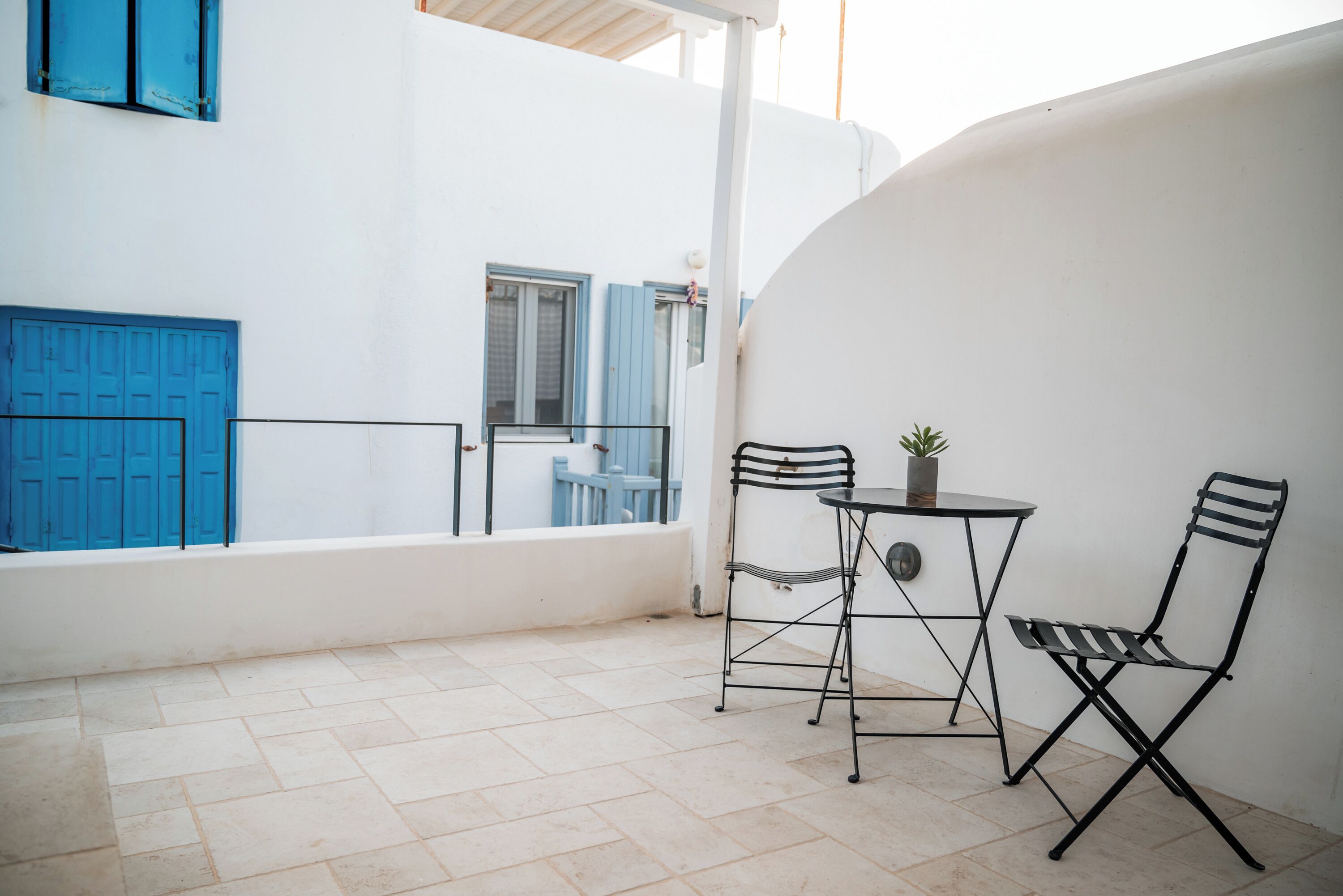 A small outdoor patio with a table and two chairs, a potted plant, and a blue door.