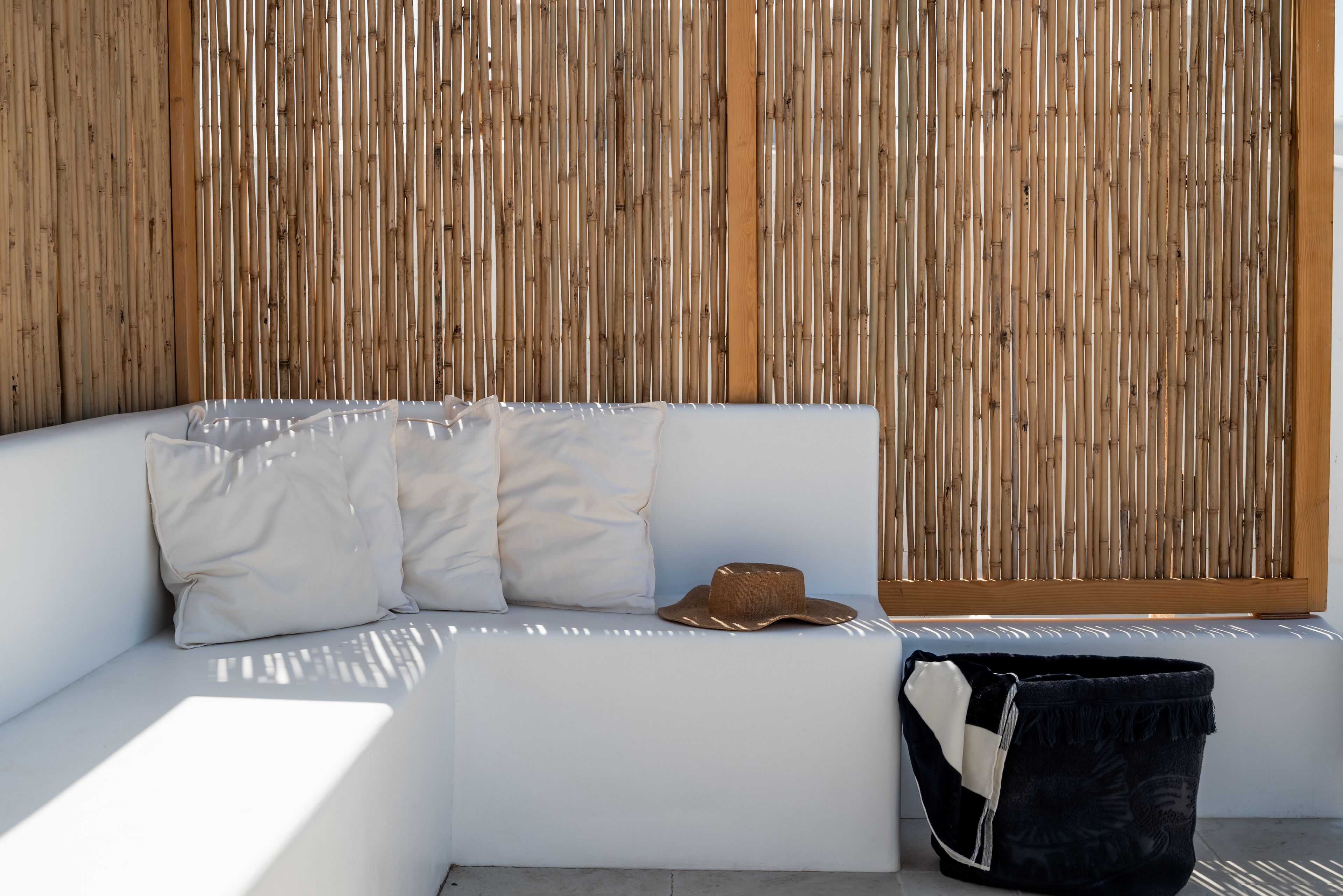 A white sofa with cushions and a hat, positioned against a bamboo wall.