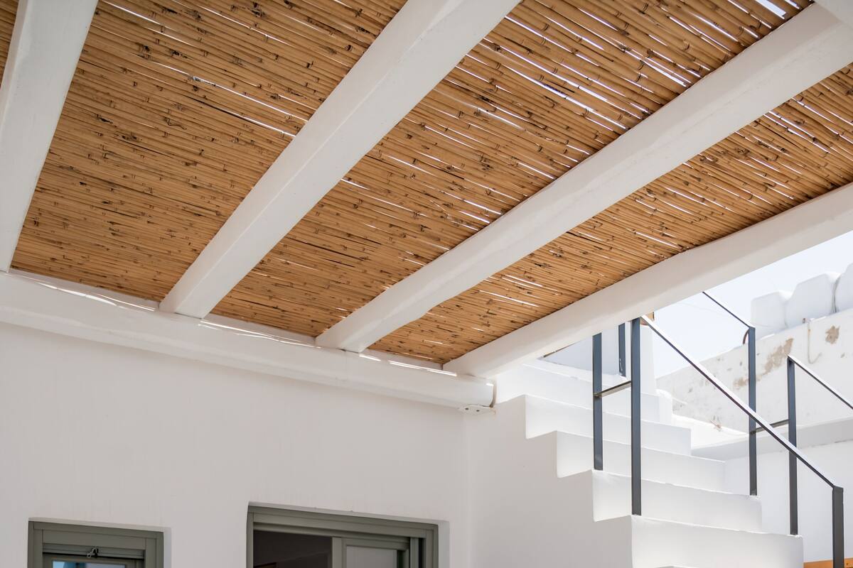 A modern interior with a wooden ceiling, a staircase, a window, and a table with chairs.