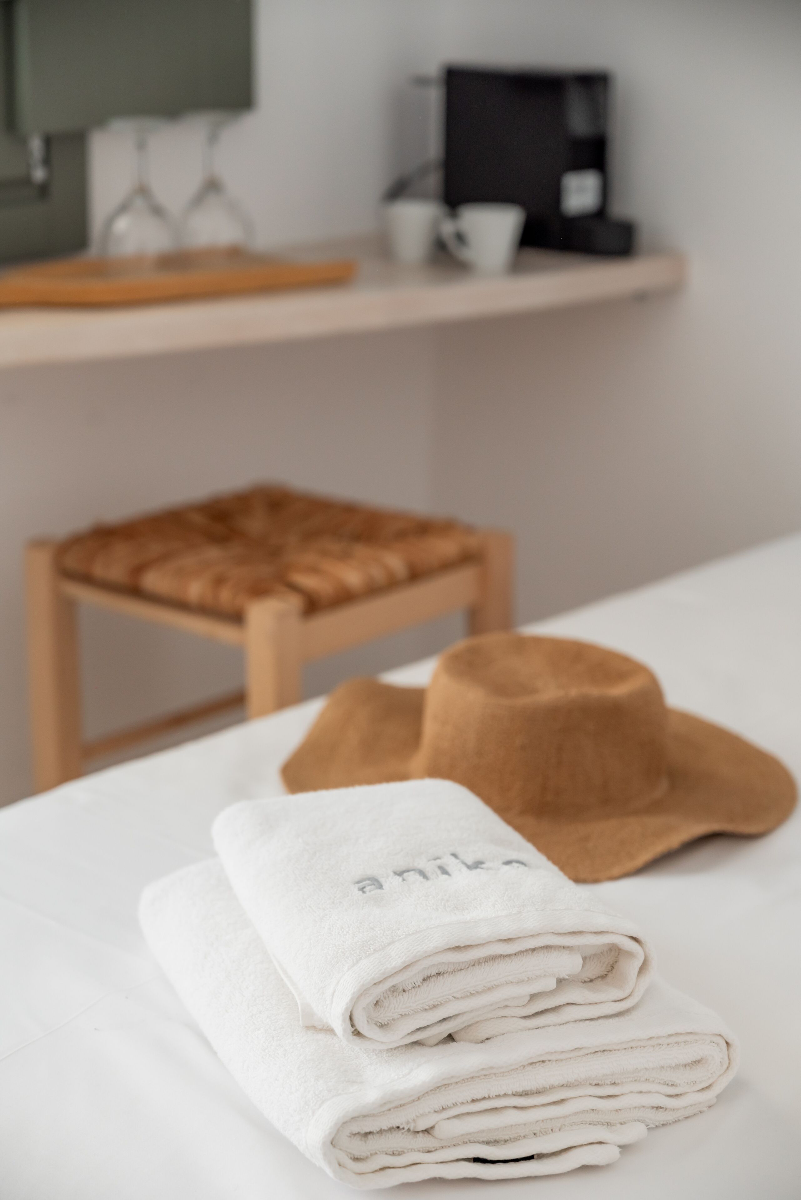 Una cama bien hecha con toallas blancas dobladas y un sombrero marrón encima.