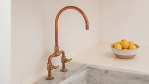 Una cocina con encimera de mármol, grifo de cobre y un cuenco de limones.
