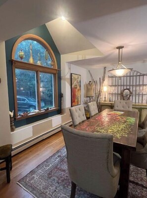 A dining area with a large table, chairs, a window with decorative items, and a chandelier.