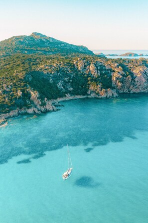 Un voilier sur une mer turquoise, avec une côte rocheuse et des collines verdoyantes en arrière-plan.