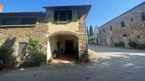 Edifici de pedra amb una entrada central arquejada, un petit porxo i una carretera de grava.