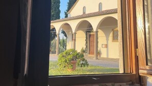 Vista per una finestra d'un edifici amb un pati central, passadissos arquejats i un penya-bàns.