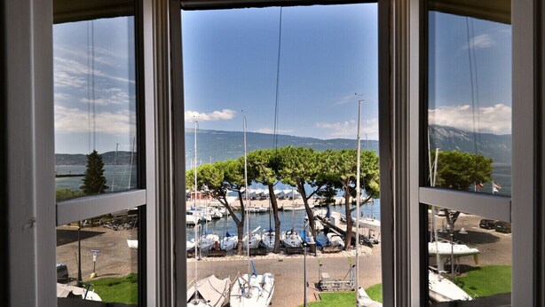 Vista a través de una ventana de un puerto deportivo con barcos amarrados, árboles y cielo despejado.