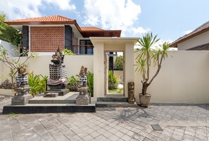 A courtyard with a statue, a potted plant, and a building with a tiled roof.