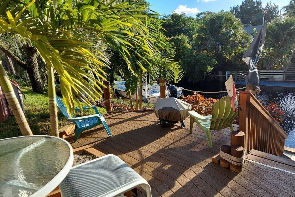 A wooden deck with outdoor furniture, a covered table, and a boat docked in the background.